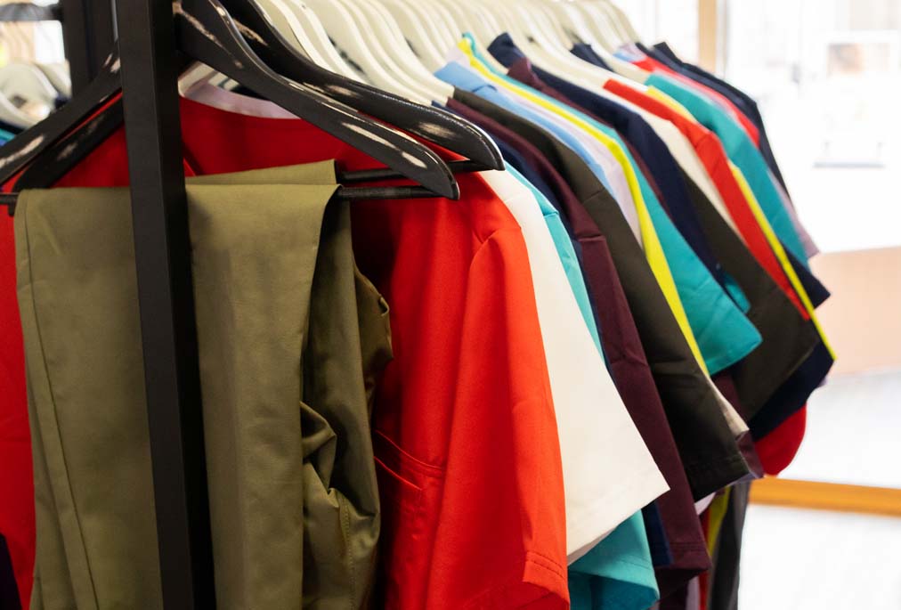 Bunte Kasacks und passende Hosen in verschiedenen Farben auf Kleiderbügeln.