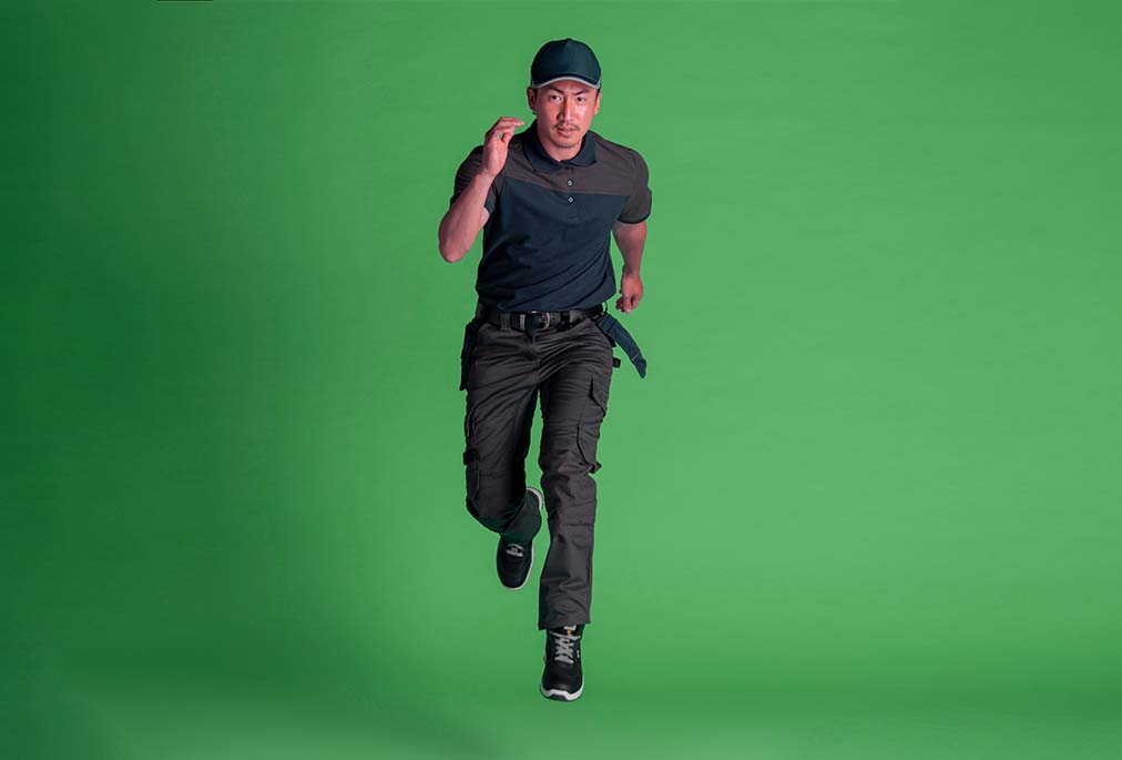 Mann in dunkler Cordura Arbeitshose und Polo-Shirt rennt vor grünem Hintergrund.