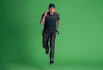 Mann in dunkler Cordura Arbeitshose und Polo-Shirt rennt vor grünem Hintergrund.