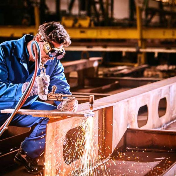 Schweißer in blauer Schutzkleidung und Schutzbrille beim Brennschneiden von Metall.