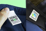 Nahaufnahme von Textiletiketten "Grüner Knopf" und "Fairtrade Cotton" auf nachhaltiger Arbeitskleidung.