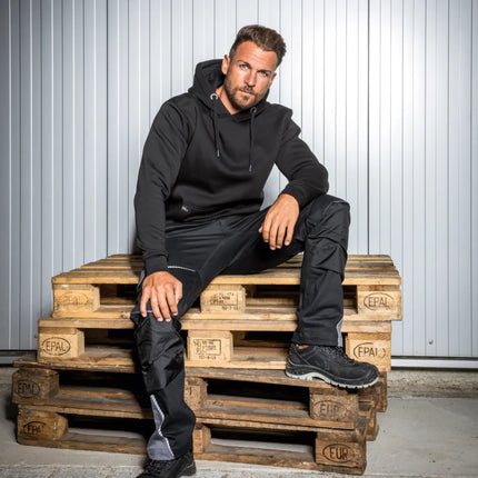 Mann trägt schwarze Leibwächter FLEX Bundhose mit Stretch, Knietaschen und Reflektoren.