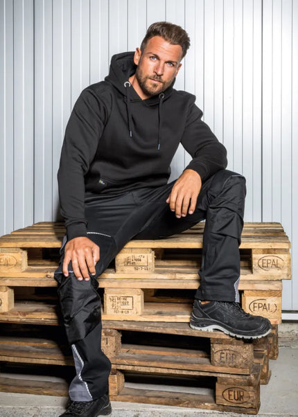 Mann trägt schwarze Leibwächter FLEX Bundhose mit Stretch, Knietaschen und Reflektoren.